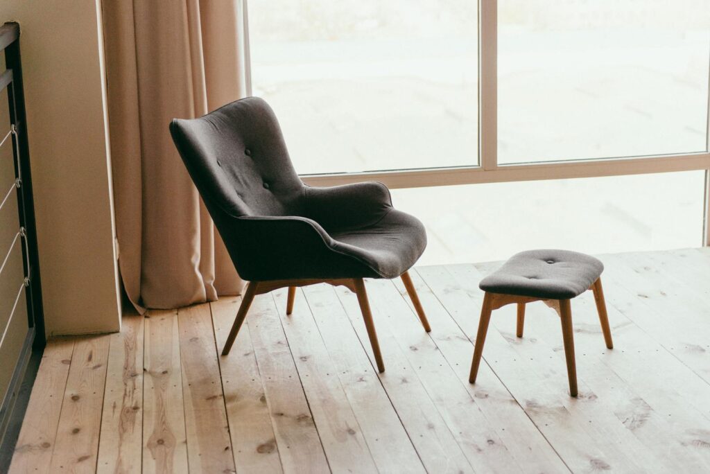 A contemporary armchair and footstool in a minimalistic room with sunlight streaming through large windows.